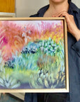Taiteilija Jenni Pennanen pitelee Candy Field -canvas-taulun mallikappaletta tammikehyksellä