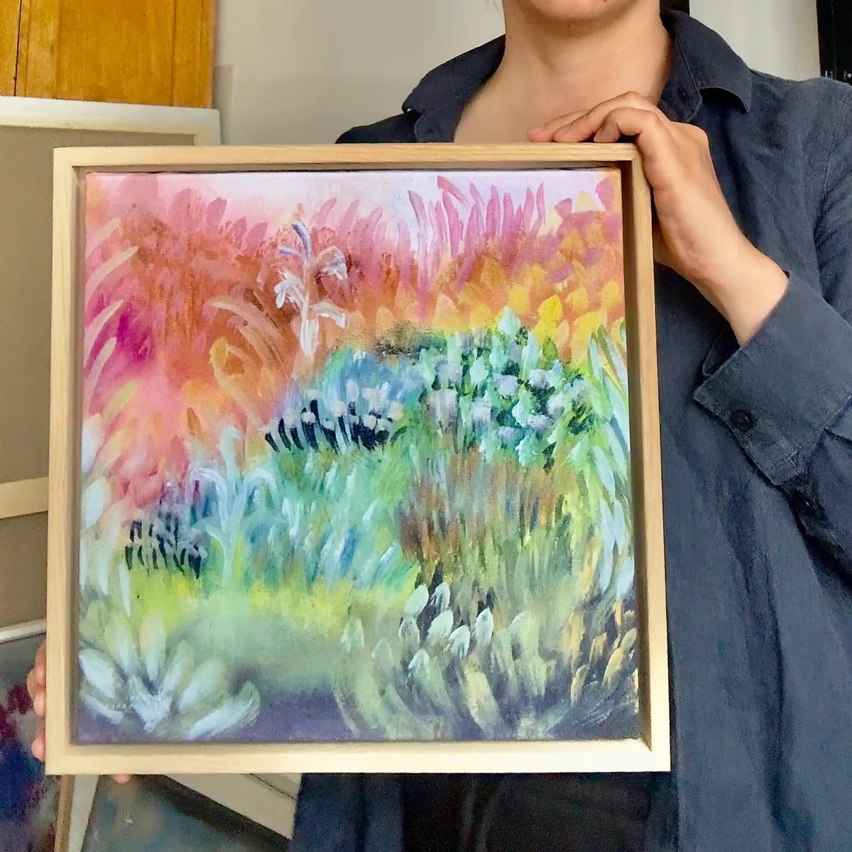 Taiteilija Jenni Pennanen pitelee Candy Field -canvas-taulun mallikappaletta tammikehyksellä